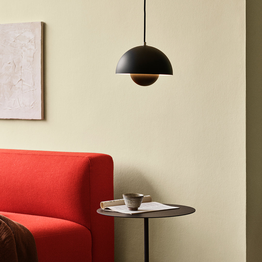 Black and wood pendant lamp above a sleek black side table, contrasted by a vibrant red sofa against a soft beige wall.