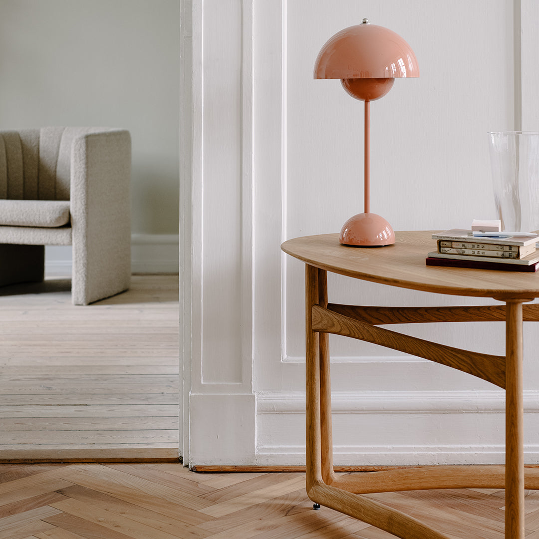 Modern wooden table with a light oak finish, a pink dome lamp, and soft neutral tones in the background.