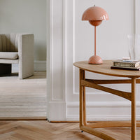 Modern wooden table with a light oak finish, a pink dome lamp, and soft neutral tones in the background.