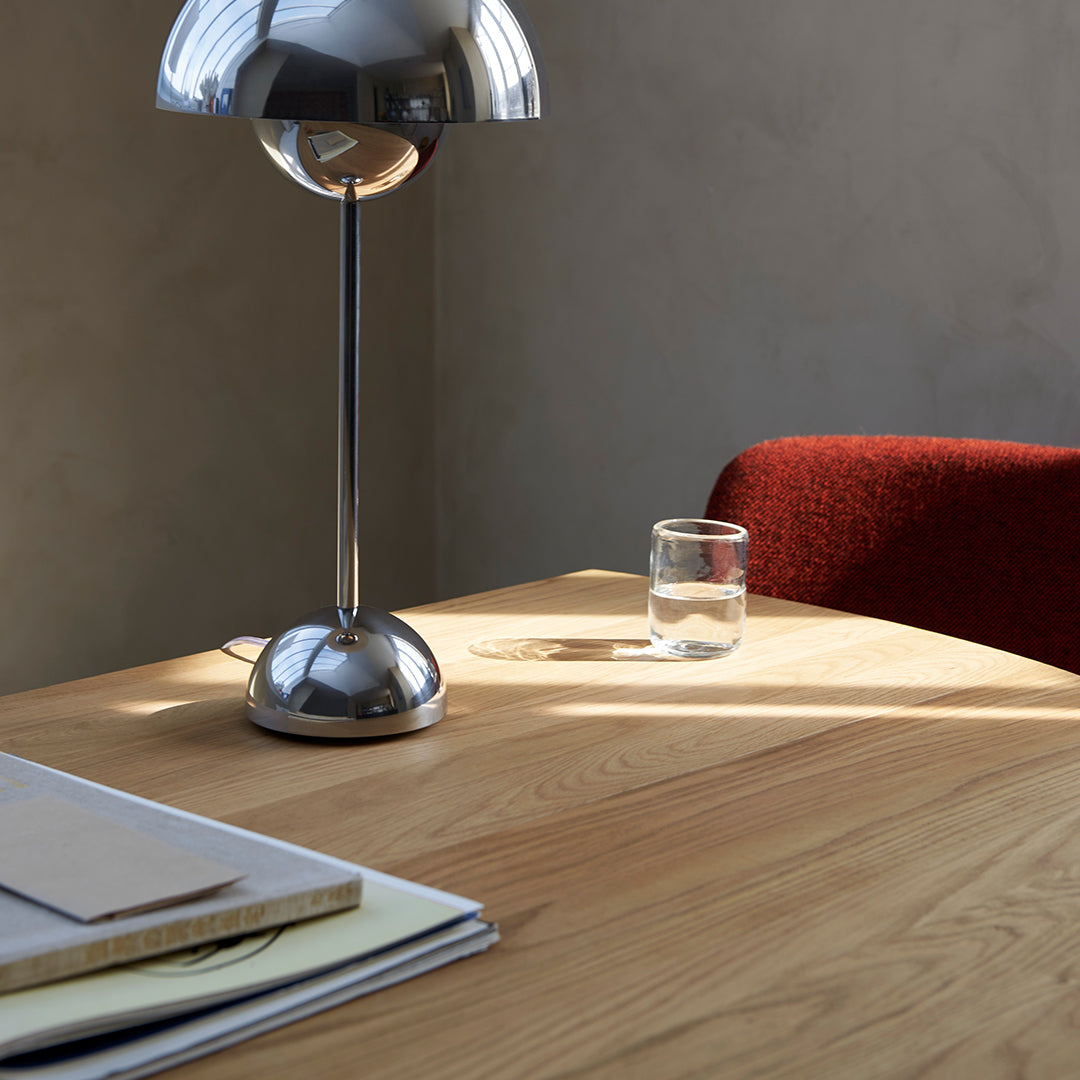 Modern table with warm oak wood, sleek silver lamp, and rich red chair against a neutral wall. Minimalist design.