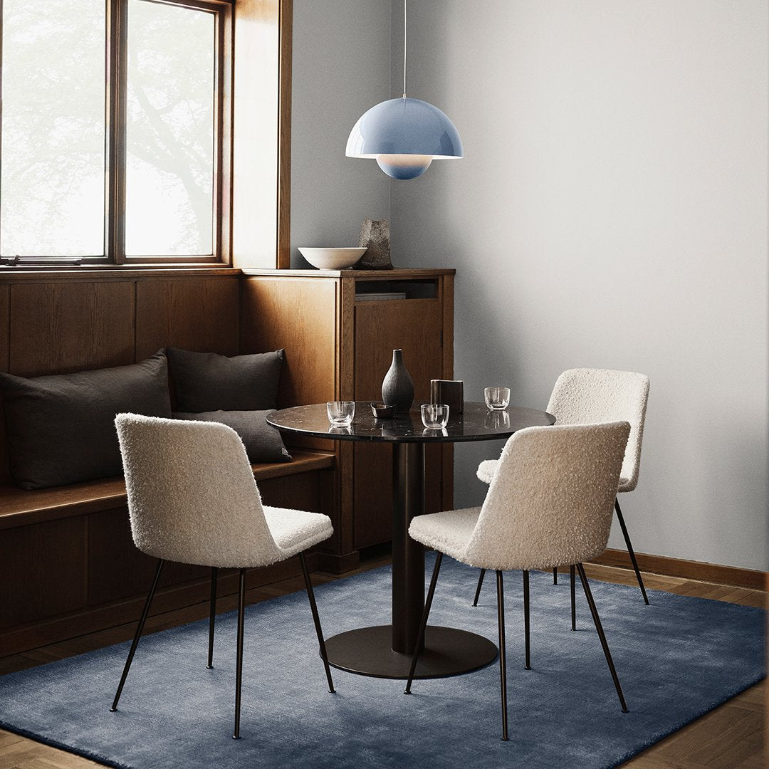 Light blue pendant lamp, neutral-toned chairs, dark table, and a soft blue rug in a cozy dining setting.