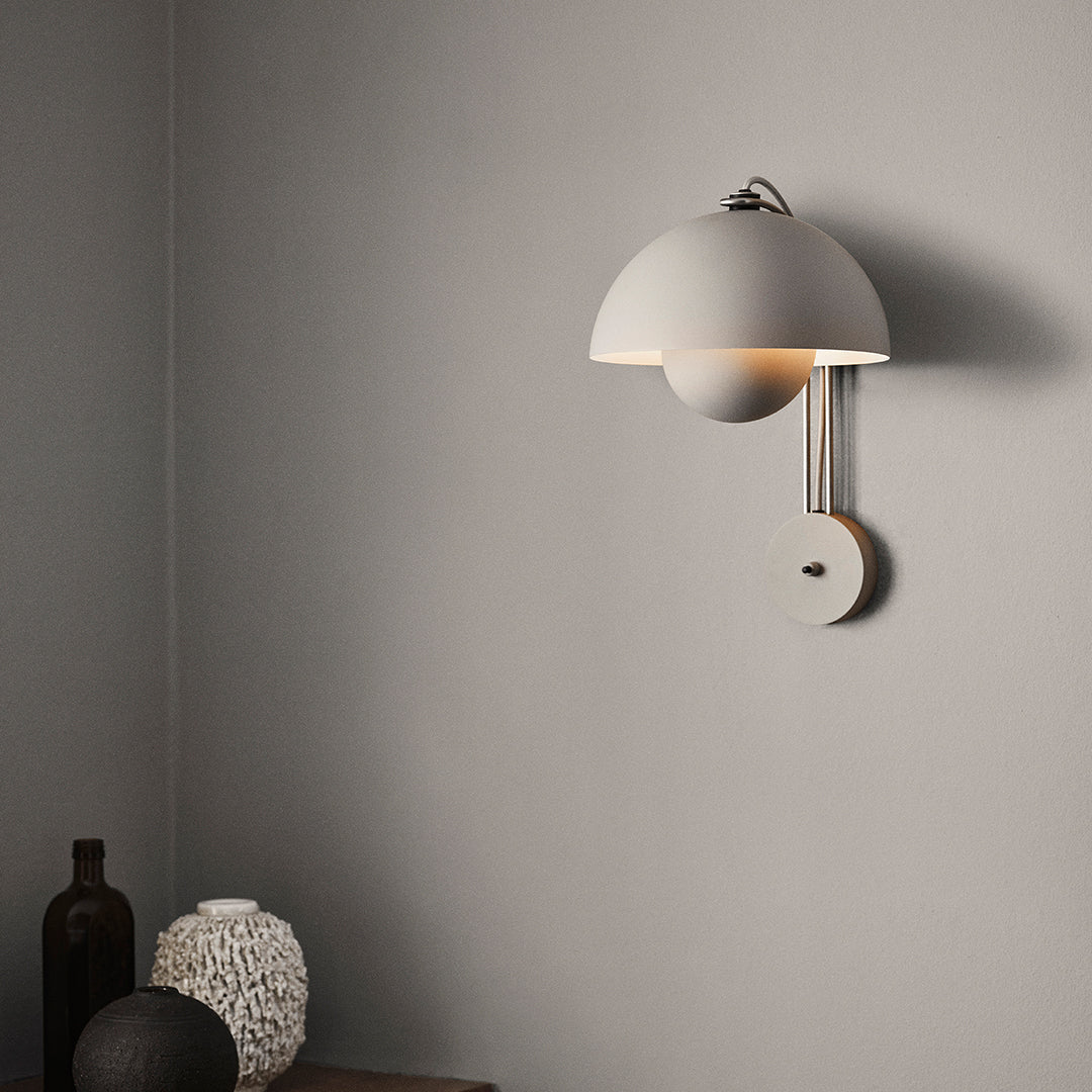 Modern white wall lamp with a circular shade and sleek design, casting a warm glow against a gray wall.