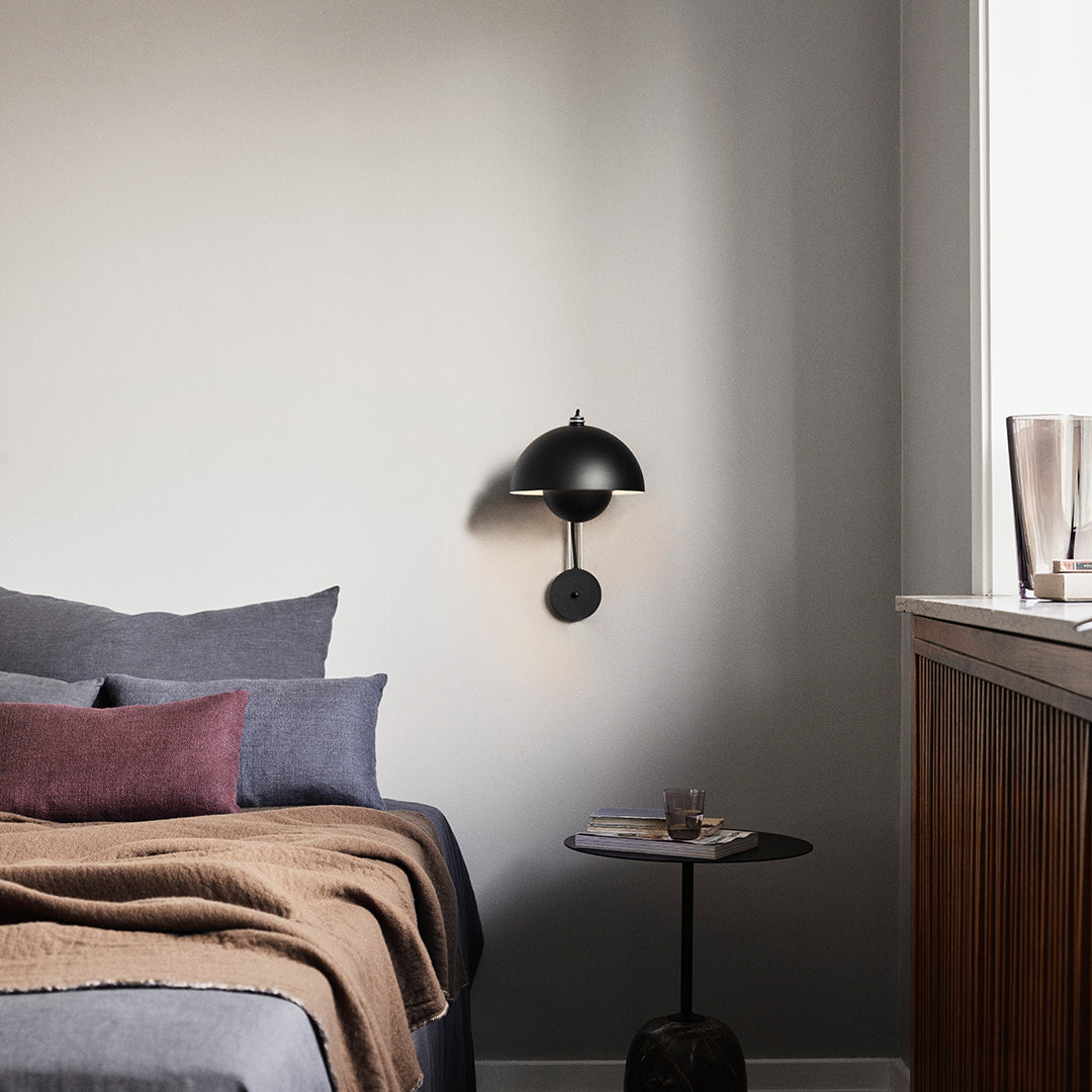 Black wall sconce with a round shade, gray bedding with a textured throw, and purple accents on a cozy side table.