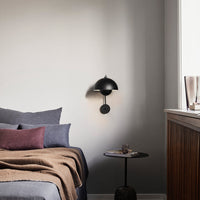 Black wall sconce with a round shade, gray bedding with a textured throw, and purple accents on a cozy side table.