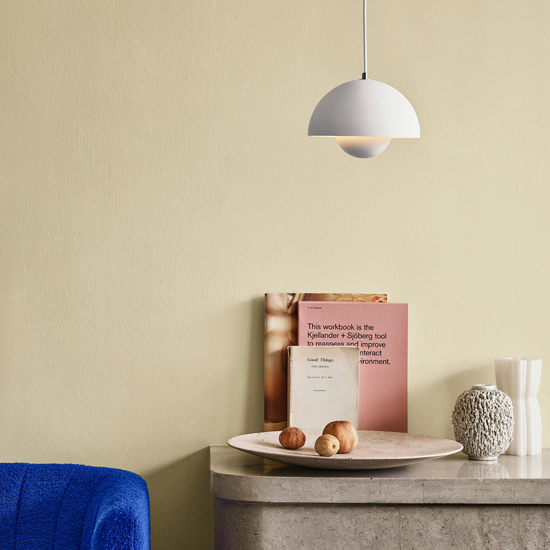 White pendant lamp against a soft yellow wall, complemented by a blue accent chair and neutral-toned decor.