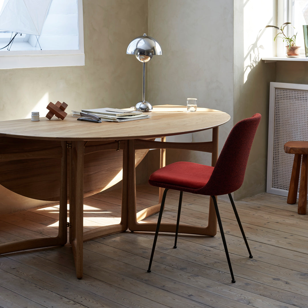 Red upholstered chair with black legs, light wood table, and neutral-toned walls create a modern, warm atmosphere.
