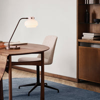 Elegant white lamp with a glass shade, brown wooden desk, neutral fabric chair, and blue textured rug. Modern home office decor.