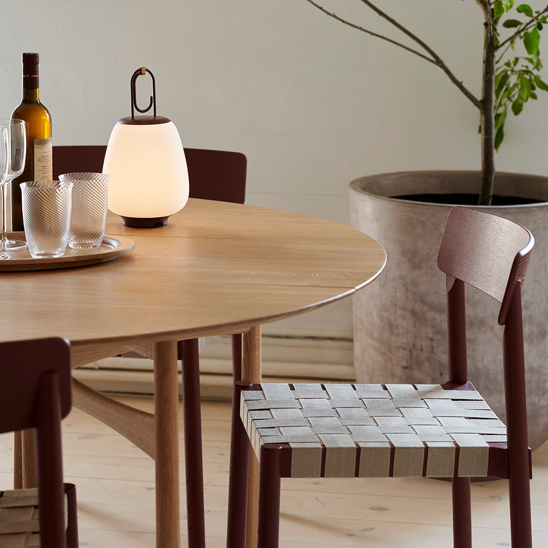 "Natural wood table with red-brown chairs and a woven, striped seat pattern, complemented by a soft, glowing lamp."