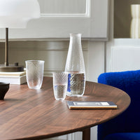 Clear glass water carafe and tumblers with diamond-patterned design on a wooden table. Light reflections enhance elegance.