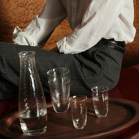 "Clear glassware set with intricate diamond patterns, displayed on a wooden tray against a warm backdrop."