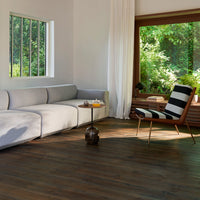 Modern living room with a light gray sectional sofa, striped black and white chair, and rich brown wooden flooring.