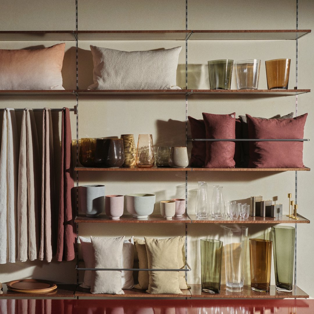 Shelves with soft pink, muted earth tones, green glassware, and textured fabric pillows in warm, natural hues.