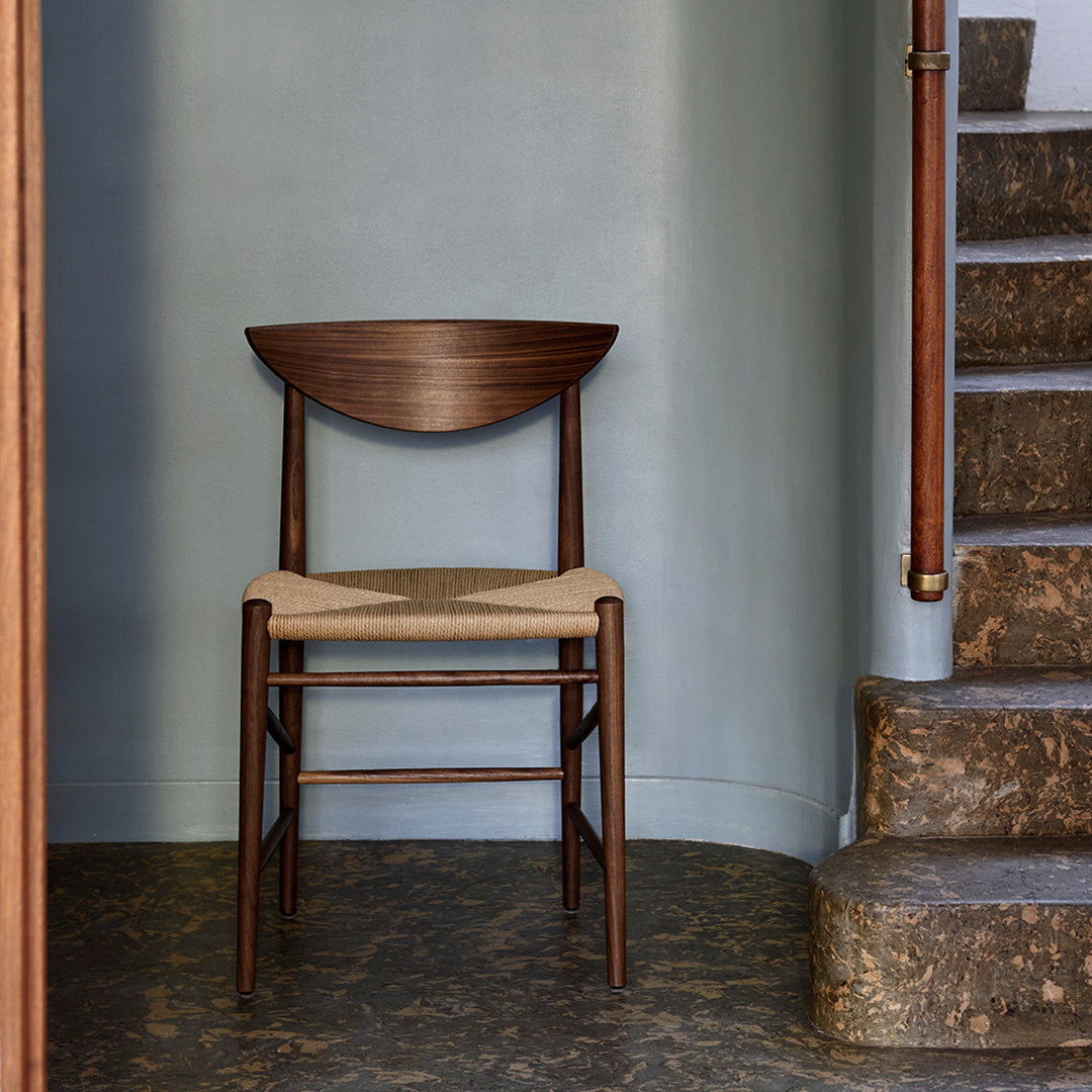Brown wooden chair with a curved backrest and woven seat, set against a light blue wall and stone stairs.