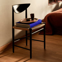 Black chair with a wooden seat, blue book, and a rustic bowl, set against warm tones and natural textures.