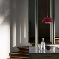 Round, burgundy pendant light casts soft shadows in a minimalist, modern interior with neutral tones and polished surfaces.
