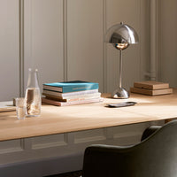 Wooden desk with a light natural finish, silver lamp, and colorful books in blue and beige tones. Clean, modern aesthetic.