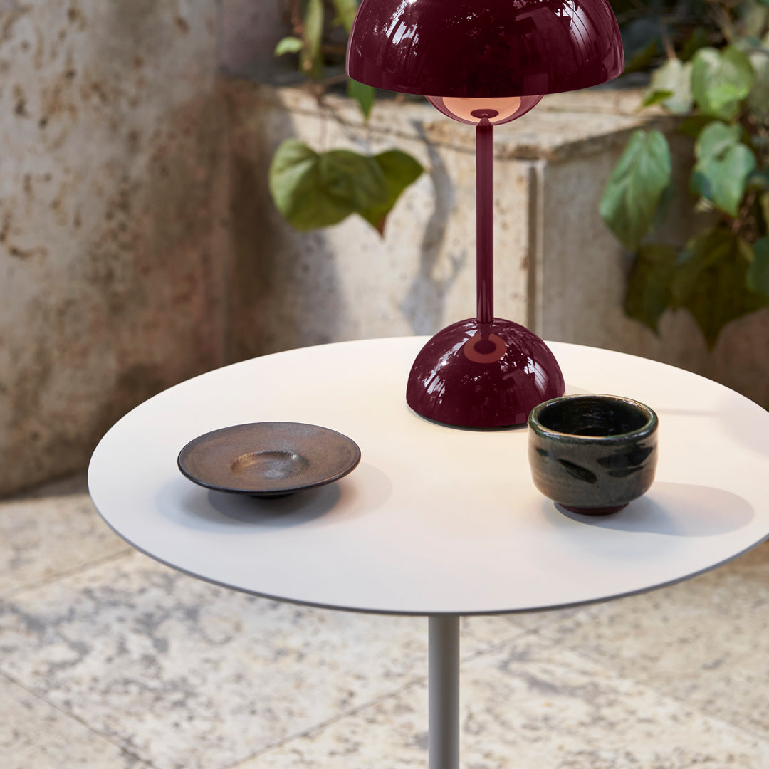 White round table with a glossy burgundy lamp, a black plate, and a textured dark green ceramic cup.