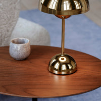 Gold lamp base on a wooden table with a gray ceramic cup, set against a soft blue rug background.