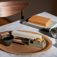 Wooden tray with dark earthy tones, bright orange and gray stationery, and a black ceramic cup on a marble surface.