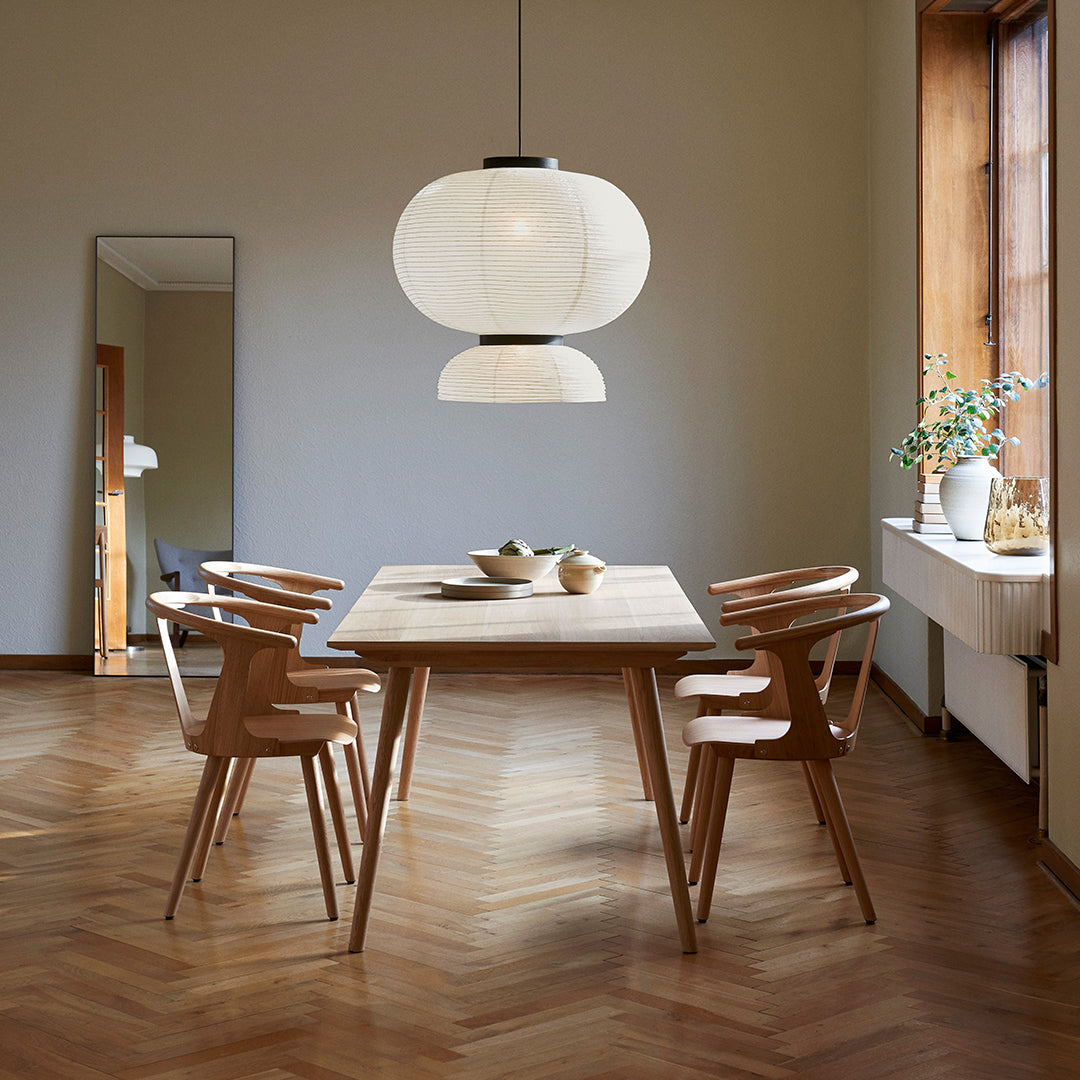 Elegant wooden dining table with natural finish, paired with minimalist chairs and soft white pendant light, featuring herringbone flooring.