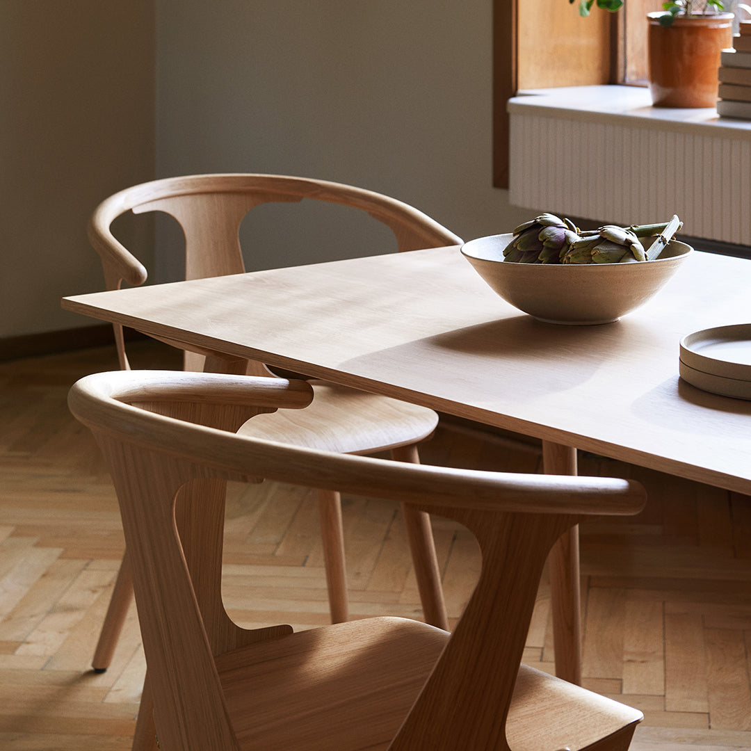 Natural wood dining table with curved chairs, featuring light tones and a smooth finish, set in a cozy room.