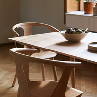 Natural wood dining table with curved chairs, featuring light tones and a smooth finish, set in a cozy room.