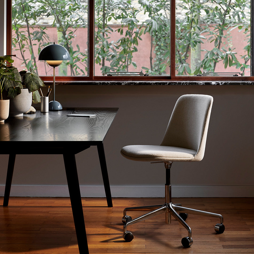 Sleek beige office chair with a smooth finish, set against a modern black desk and green foliage backdrop.