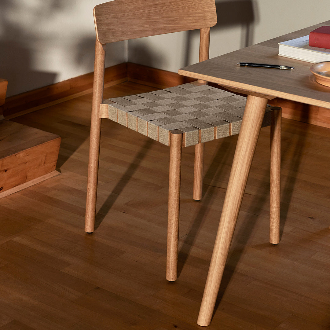 Light wood chair with a woven gray and beige checkered seat pattern, set on warm wooden flooring.