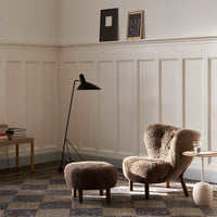 "Cozy brown accent chair and ottoman with a textured, plush pattern against a neutral-toned wall and patterned floor."