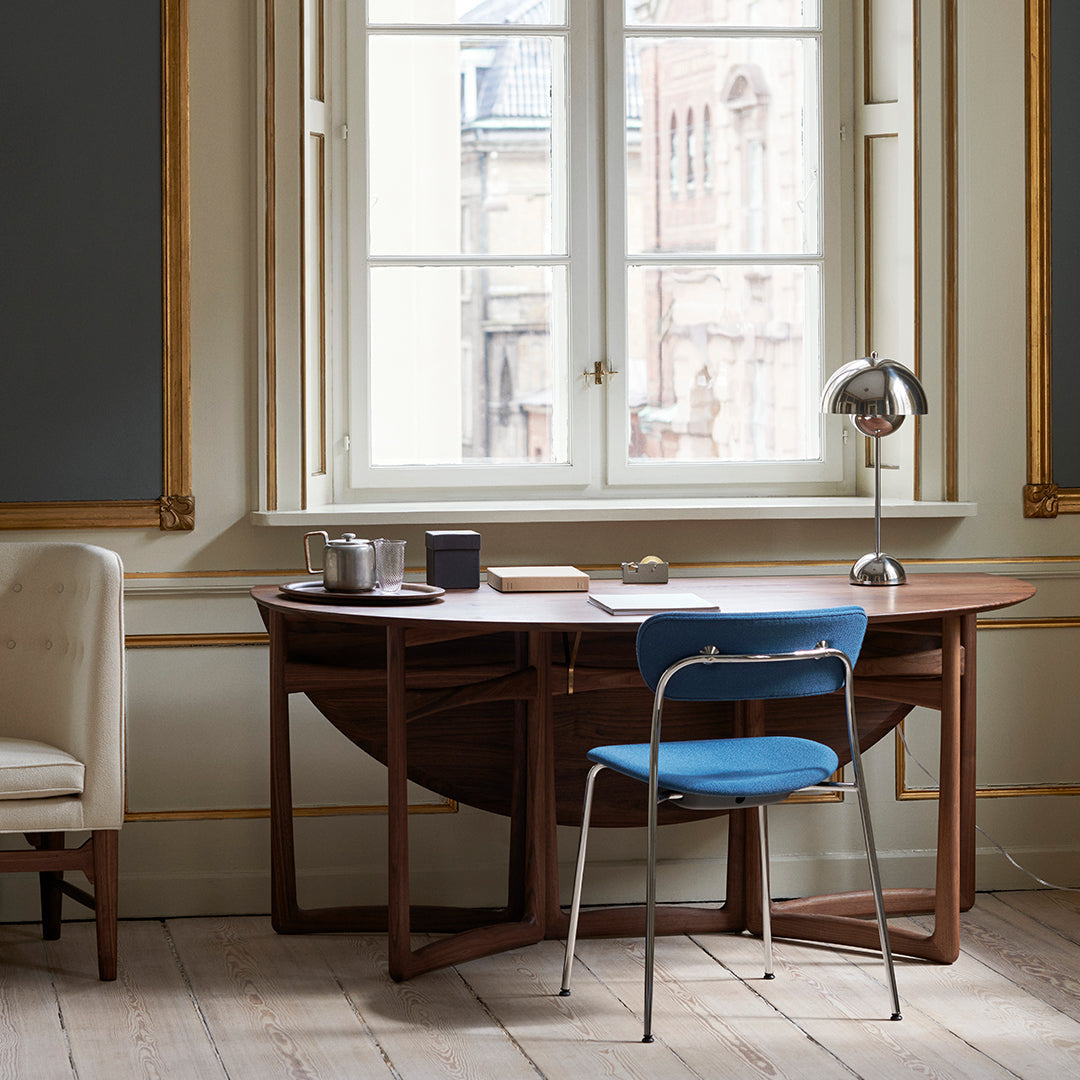 Modern wooden desk in rich brown with blue chair and soft beige accents, set against elegant neutral wall and window.