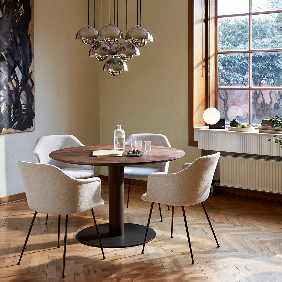 Round wooden table with a rich brown finish, complemented by light-colored fabric chairs and metallic accents.