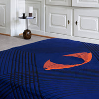 Navy blue quilted bedspread with orange abstract swirl design and linear patterns for a modern look.