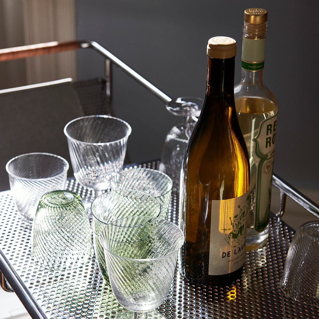Clear ribbed glassware with green and amber bottles on a metallic cart, showcasing elegant patterns and textures.