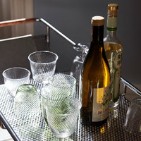 Clear ribbed glassware with green and amber bottles on a metallic cart, showcasing elegant patterns and textures.