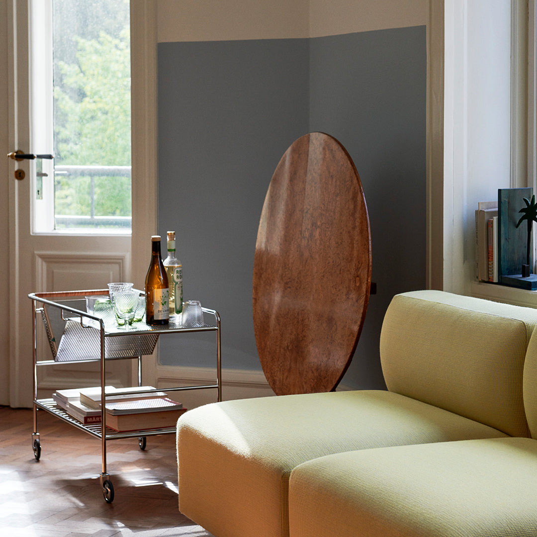 Light grey wall, earthy wood table, soft yellow couch, and glassware create a modern, inviting interior scene.