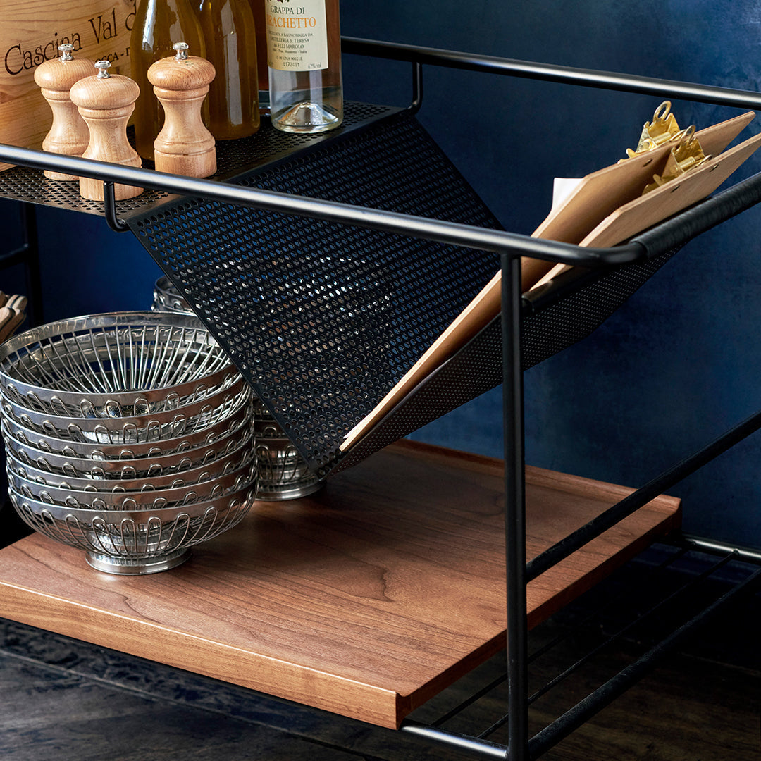 Stylish black metal cart with wooden shelf, featuring circular silver bowls and a textured black mesh compartment.