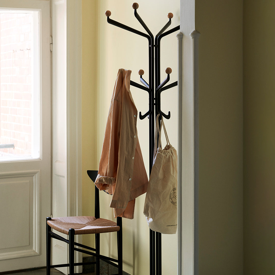 Black coat rack with wooden pegs, featuring a soft beige jacket and cream bag against a light yellow wall.