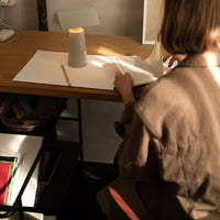Warm-toned workspace with a brown coat, neutral papers, and a gray cup on a wooden table. Soft lighting enhances colors.