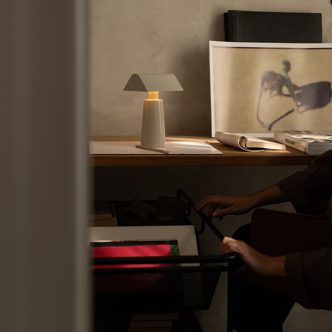 Stylish table lamp with soft white shade, warm glow, and natural wood on a minimalist desk with neutral wall backdrop.