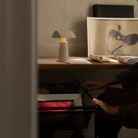 Stylish table lamp with soft white shade, warm glow, and natural wood on a minimalist desk with neutral wall backdrop.