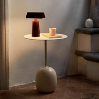 "Modern round side table in beige with a sleek white top, accented by a brown lamp and pastel-colored decor."