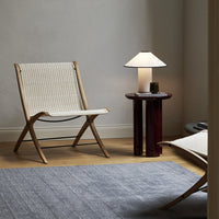 Natural woven chair in light beige, paired with a white lamp and a textured gray rug, creating a calming interior look.
