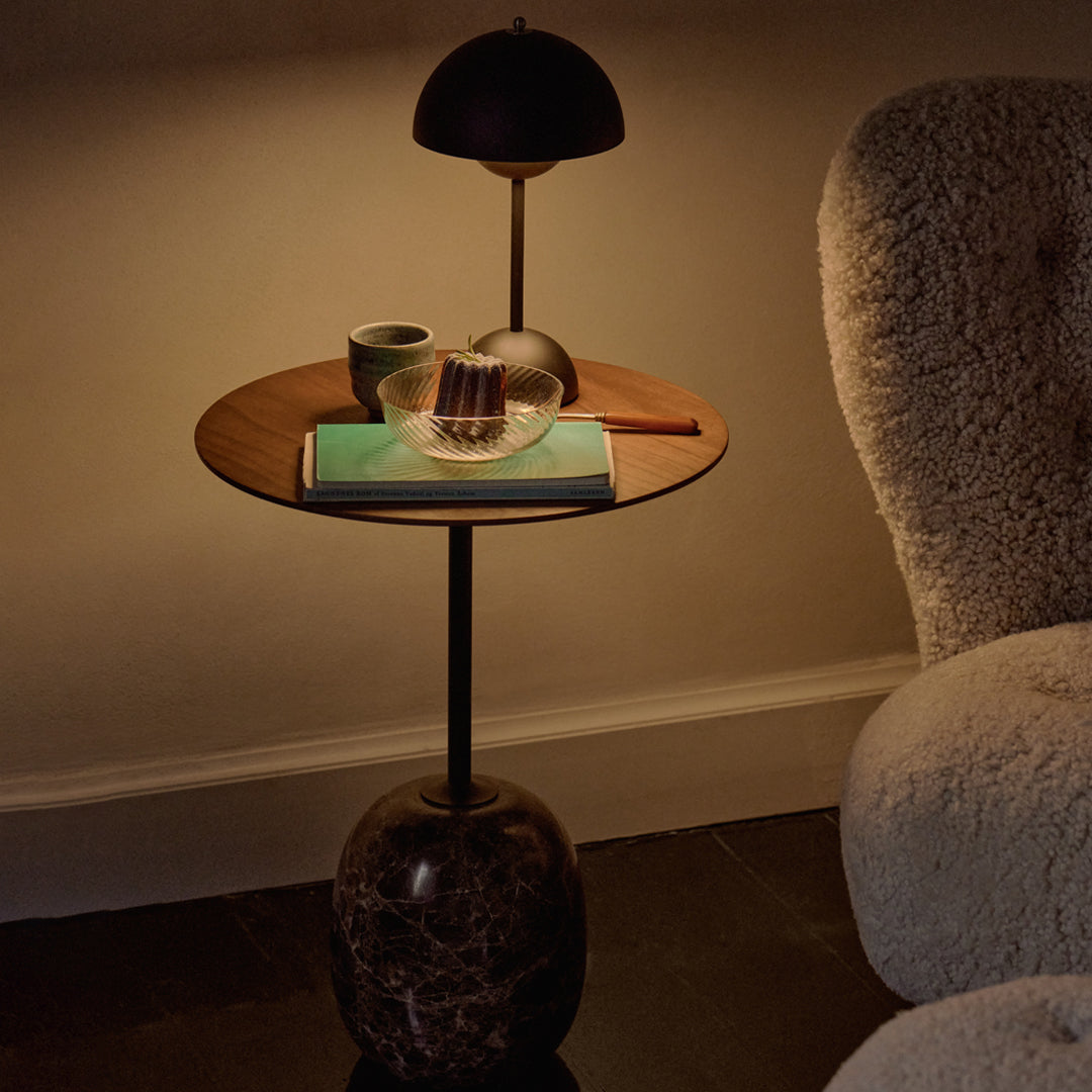 Modern side table with a wooden top, dark marble base, and minimalist decor, featuring earthy tones and soft illumination.