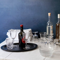 Clear glassware with textured patterns on a black tray, set against a blue background and white tablecloth.