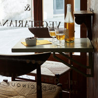 "Light green table with yellow accents and patterned seat; two glasses of golden drink by the window."