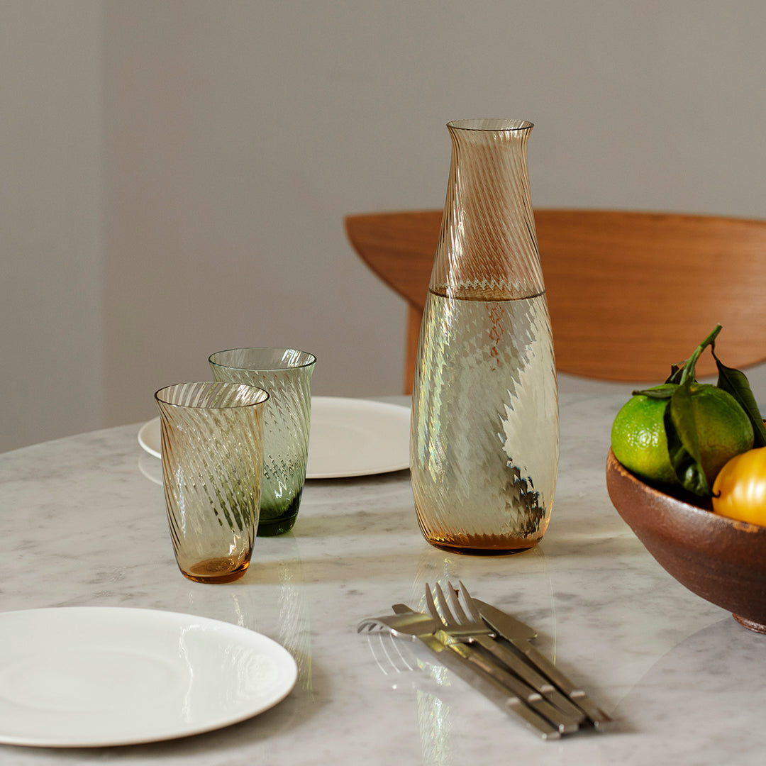 Textured green and amber glass carafe and tumblers with a decorative diamond pattern on a marble table.