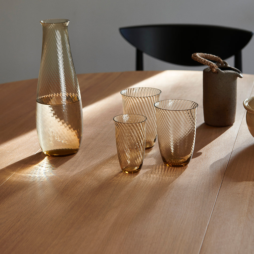 "Amber glass carafe and tumblers with textured ribbed patterns on a wooden table."
