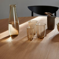 "Amber glass carafe and tumblers with textured ribbed patterns on a wooden table."