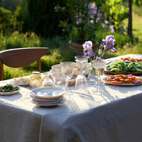 "Elegant outdoor dining table with white linens, clear glassware, and colorful plates of vibrant greens and reds."