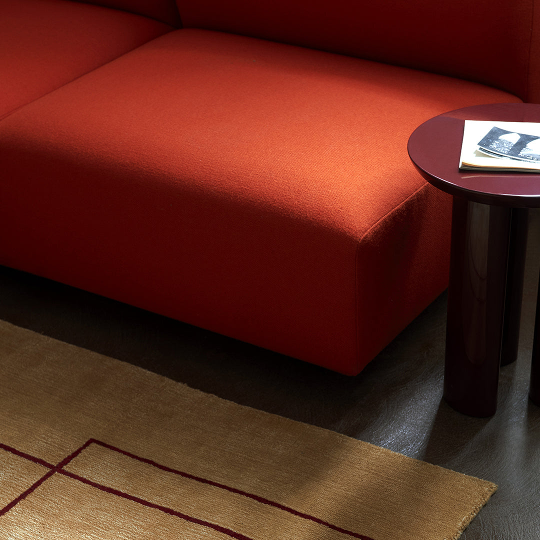 Vibrant orange sofa with a textured surface, paired with a dark table and a geometric patterned rug in neutral tones.
